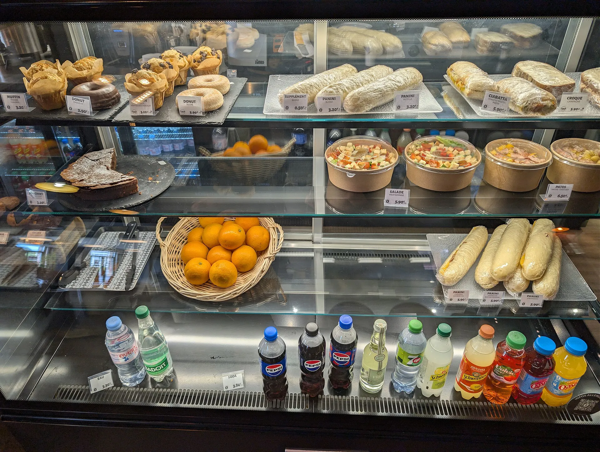 A glass display case in a small cafe holds pastries, sandwiches, salads and bottled drinks for customers.