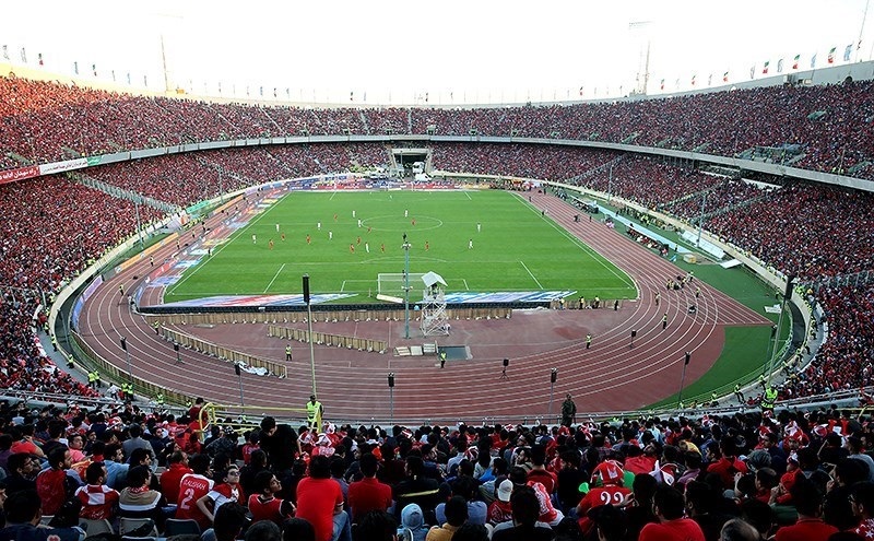 A packed stadium crowd watching sport beneath large illuminated screens